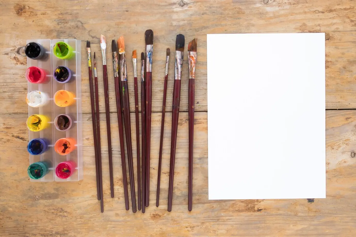 Ein weißes Blatt Papier neben Gouache und Malpinseln.